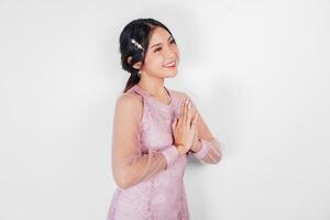 simpático asiático mujer vistiendo rosado vestir es dando gestos de tradicional saludos por su manos foto