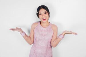 A cheerful Asian woman wearing pink dress is pointing copy space beside her, isolated by white background. photo