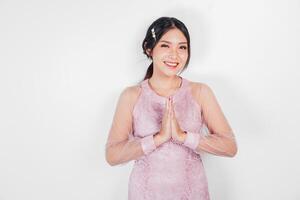 Friendly Asian woman wearing pink dress is giving gestures of traditional greetings by her hands photo