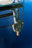 Person Enjoying Serene Waterfront View. A person standing on a dock with their feet in the water photo