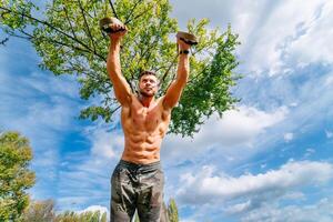 A Strong Man Showing Off His Strength. A shirtless man holding a pair of dumbs above his head photo