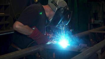 trabajador con protector máscara soldadura metal. un hombre soldaduras un metal con un soldadura máquina. soldador es trabajando a el fábrica y soldadura un metal construcción. soldadores trabajando a el fábrica hecho metal video