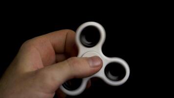 manlig hand med vit spinnare isolerat på svart bakgrund. vit fidget spinnare enhet på svart bakgrund. spelar med en vit hand spinnare fidget leksak. vit spinnare i man hand på svart bakgrund video