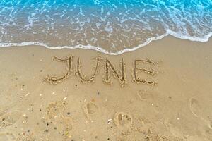 The word June is written on the sand of a beach by the sea. Washed off by a wave. The inscription disappears. End of summer concept. Back to school. photo