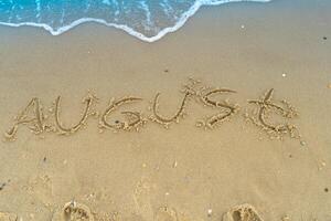 el palabra agosto es escrito en el arena de un playa por el mar. lavado apagado por un ola. el inscripción desaparece final de verano concepto. espalda a escuela. foto