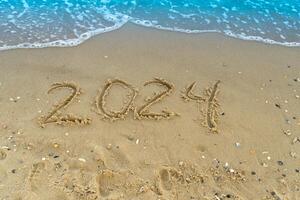 The numbers 2024 are written on a sandy seashell beach. Wave and surf. Summer New Year. Vacation, resort and recreation. Nature. Sea coast photo