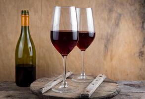 Two glasses of red wine. The bottle of wine is on the table. Wine background. Still life. Alcoholic drink in a glass. Wooden background photo
