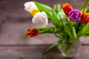 Vase with multi-colored bouquets of tulips on a wooden table. Tulip with dew drops. Selective focus. Copy space. Spring background. Tulips with dew drops. photo