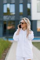 Side view portrait of a beautiful blonde woman holding a phone and laughing while talking on the phone against the background of the city. photo