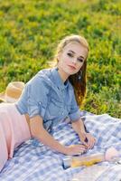 Stylish young woman with bright makeup in a denim shirt is resting on a plaid in the open air photo