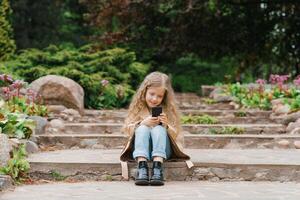 Seven year old girl communicates online on a smartphone, sitting in nature in the spring in the park photo