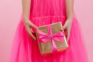 cerca arriba de un niña participación un regalo caja con un rosado seda cinta, dando un regalo para un día festivo. alegre Navidad, contento nuevo año, San Valentín día, día festivo, festivo, cumpleaños, sorpresa concepto. foto