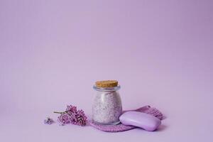 Aromatic spa set. Sea salt for body care, natural soap and lilac flowers on a purple background photo