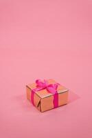 Gift box in gold paper decorated with fuchsia bow on pink background with copy space photo