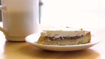 Cake and tea on the table by the window in the coffee shop. Selective focus. Coffee and raspberry scone on wooden table. Lipstick on mug with sunny window light behind. video