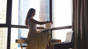 elegant zakenvrouw freelancer begint werken met laptop, ze is zittend Aan de tafel, genieten van panoramisch visie in de stad achtergrond. laag sleutel video. hoog kwaliteit 4k beeldmateriaal video