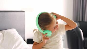 Little girl enjoying music using green kids headphones in home bed. High quality 4k footage video