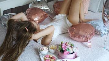 magnifique Jeune fille à Accueil sur le lit dans le Matin prendre plaisir valentines journée fête avec cœur en forme de des ballons. haute qualité 4k métrage video