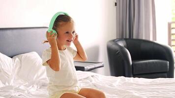 liten flicka lyssnande musik använder sig av grön barn hörlurar i Hem säng. hög kvalitet 4k antal fot video