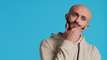 Thoughtful person being puzzled about a decision, standing over blue background in studio and thinking. Pensive middle eastern man being uncertain and doubtful about something. Camera 2. video