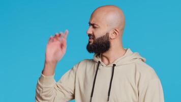 Arab male model doing no symbol on blue backdrop, showing his rejection and denial in studio. Middle eastern guy expressing refusal with a negative gesture, serious man. Camera 2. video