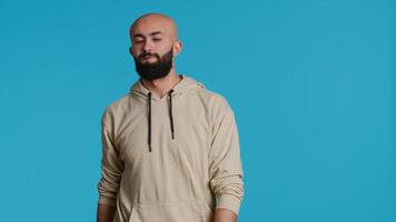 Middle eastern man raises palm and says no in studio, expressing his rejection with stop symbol over blue background. Negative person showing denial and restriction. Camera 1. video