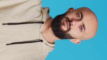 Vertical Video Young musician posing as a choir conductor in studio, conducting tunes for a band at classical show. Middle eastern person acting as bandmaster, serious expression over blue background. Camera 2.