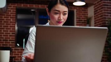 mujer de negocios haciendo computadora Tareas para equipo proyecto en oficina durante la noche, leyendo información en pantalla. panorámica Disparo de trabajador trabajando tarde a noche, mecanografía en ordenador portátil teclado, cámara si video