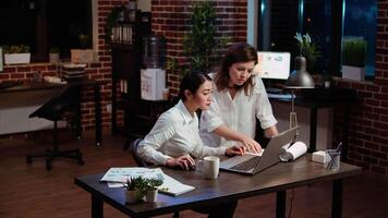 Employee and coworker working together on project at laptop, solving tasks late at night, celebrating positive feedback from management. Excited colleagues doing high five after seeing good results video