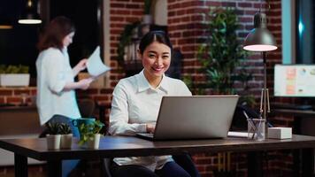 Zoom in on joyful asian employee writing important emails at computer desk, finalizing deal with business partners. Portrait close up shot of happy employee typing on laptop, camera B video