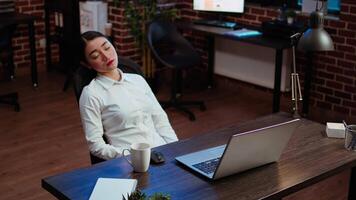 Tired employee asleep on computer desk chair suddenly waking up, struggling to finish writing emails. Drowsy businesswoman working overnight, typing on laptop, trying to stay awake, camera A video