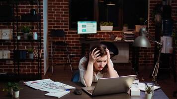 Businesswoman working on company project overnight, feeling frustrated, putting head in hands. Upset employee sighing while looking over figures on laptop screen, exasperated by failure video