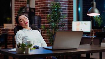 Tired employee asleep on computer desk chair suddenly waking up, struggling to finish writing emails. Drowsy businesswoman working overnight, typing on laptop, trying to stay awake, camera B video