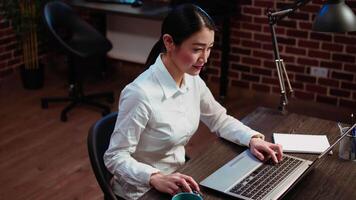 Employee enjoying cup of coffee while analyzing sales reports to plan business development. Office employee drinking hot beverage while using laptop to do project research video