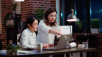 Asian staff member calling manager to her computer desk to ask for feedback on project progress. Worker in brick wall office requesting assistance from team leader during nightshift video