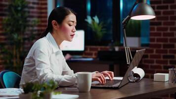 Asian employee brainstorming with coworker to compose email at computer desk, finalizing deal with business partners. Businesswoman and colleague closing agreement with associates, camera B video