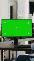 verticale video specialista guardare a schermo verde modello su del desktop tenere sotto controllo nel piccolo attività commerciale agenzia posto di lavoro. persona controllo isolato Schermo mostrando vuoto chiave cromatica modello, problema risolvendo. tripode sparo.