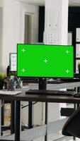 Vertical video Greenscreen monitor in coworking space running on desk, open floor plan small business office. Computer showing isolated mockup template with blank chromakey screen, modern career.