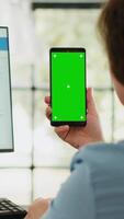 verticaal video manager houdt telefoon met groene scherm in bedrijf agentschap werkplek. zakenvrouw werken met geïsoleerd mockup sjabloon terwijl tonen blanco Chroma sleutel Scherm, opstarten baan taken.