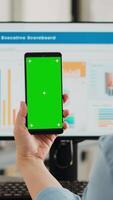 Vertical video Businesswoman showing greenscreen display in coworking space, holding device with isolated copyspace layout on screen. Person using smartphone with mockup chromakey template.