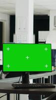 Vertical video Workstation displaying greenscreen layout with copyspace on monitor at empty desk in urban coworking space. Chromakey display equipment adopted in smaller company operations. Tripod shot.