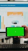 Vertikale Video Geschäft Operator Fokussierung auf leer Attrappe, Lehrmodell, Simulation Bildschirm mit Copyspace Overlay während mit isoliert grüner Bildschirm auf Handy, Mobiltelefon Telefon. Mitarbeiter Prüfung Smartphone Anzeige mit Chromakey Vorlage.