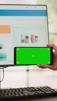 verticaal video zakenvrouw analyseren smartphone app met groene scherm sjabloon in opstarten coworking ruimte. persoon op zoek Bij geïsoleerd Chroma sleutel Scherm met mockup Aan digitaal mobiel apparaat, kopieerruimte.