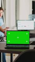 Vertical video Laptop with greenscreen display on desk in modern startup agency office, wireless computer running isolated mockup copyspace. Empty workstation with chromakey blank device.