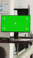 Vertical video Empty workstation with greenscreen running on computer, open floor plan coworking space presenting isolated display with chroamkey template. Monitor on desk showing blank copyspace layout.