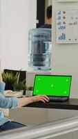 Vertical video Office employee watches greenscreen on laptop display, working on small business operations at desk. Person looking at screen running isolated chromakey template with mockup copyspace.