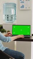 Vertical video Office worker checks greenscreen on laptop, working in small business agency. Woman looking at screen showing isolated mockup template with chromakey copyspace, coworking space.