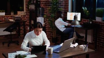 femme d'affaires vérifications croisées Les données entre financier graphiques et entreprise l'Internet site Internet, Faire Tâches pour équipe projet dans Bureau pendant la nuit. employé travaux à nuit, dactylographie sur portable clavier, caméra une video