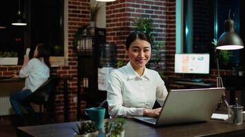 Zoom in on joyful asian employee writing important emails at computer desk, finalizing deal with business partners. Portrait close up shot of happy employee typing on laptop, camera A video