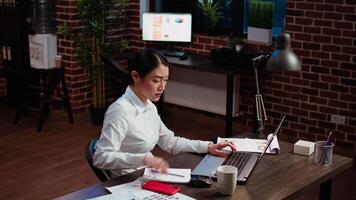 Stressed businesswoman doing multitasking, answering phone while crosschecking data between laptop and paperwork. Worker taking telephone call and comparing financial statistical graphs video